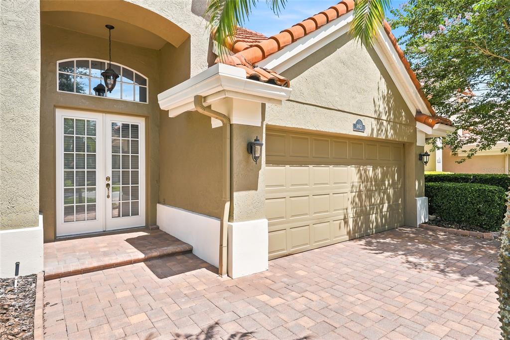 A beige stucco house exterior features a double-door entrance, a garage, and a paver driveway — 18912 PLACE MARQUETTE, LUTZ, FL