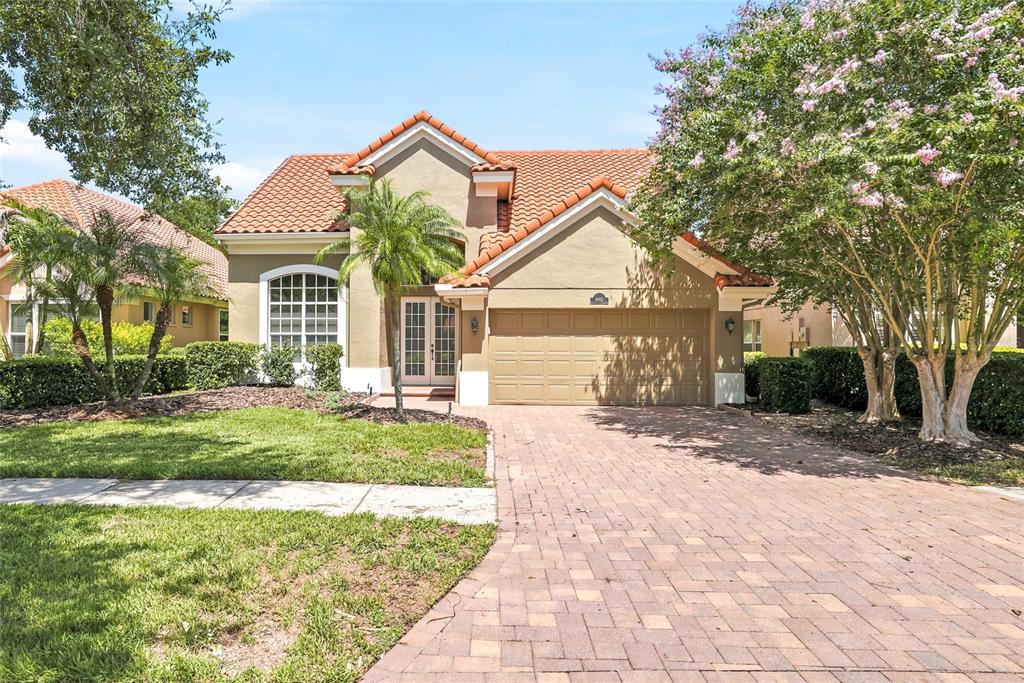 A single-story house with a tile roof, tan stucco exterior, and a brick paver driveway — 18912 PLACE MARQUETTE, LUTZ, FL