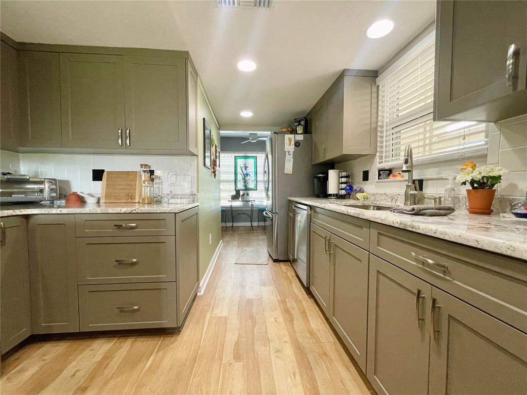 A galley kitchen features sage green cabinets, granite countertops, and light wood-look flooring — 7893 SAILBOAT KEY BOULEVARD S UNIT 101, SOUTH PASADENA, FL