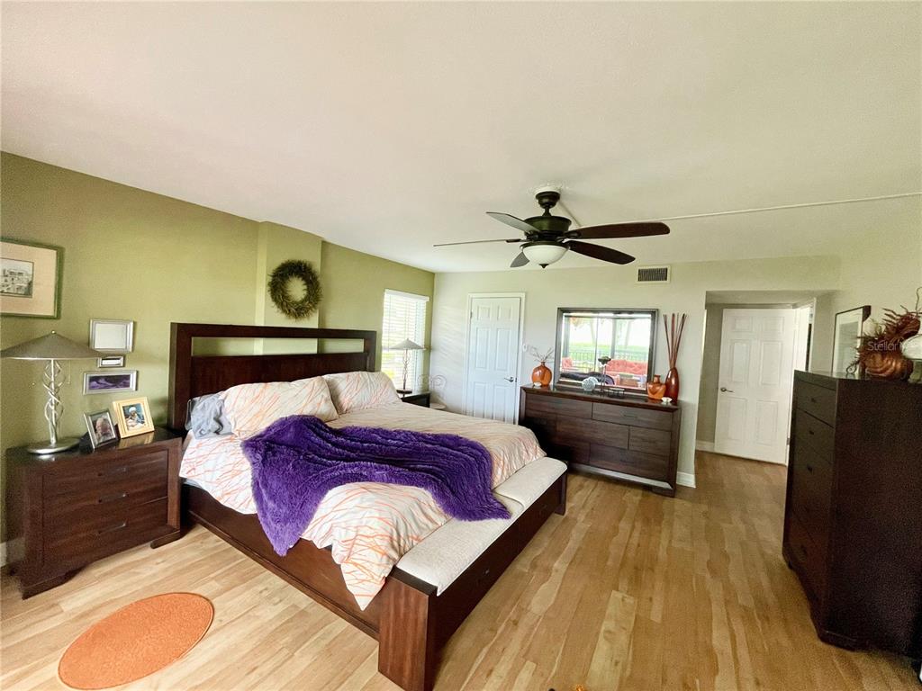 A bedroom features a dark wood bed frame, light wood flooring, and olive green walls — 7893 SAILBOAT KEY BOULEVARD S UNIT 101, SOUTH PASADENA, FL
