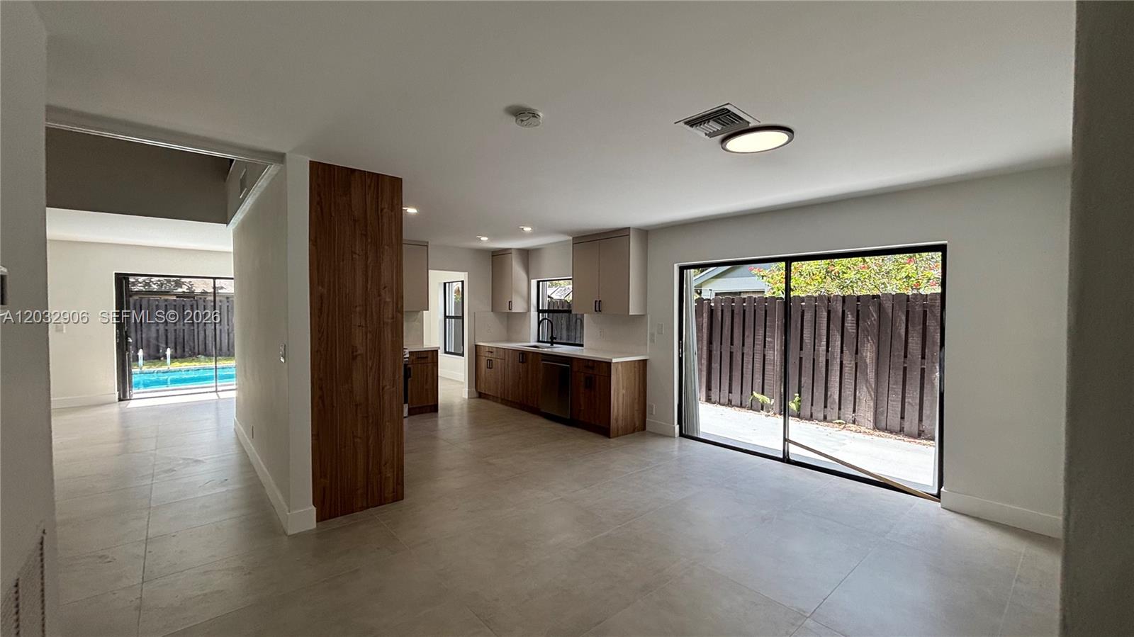 A kitchen with wood-toned cabinets and light tile floors opens to a backyard patio — 49 Forest Cir, Cooper City FL 33026, COOPER CITY, FL