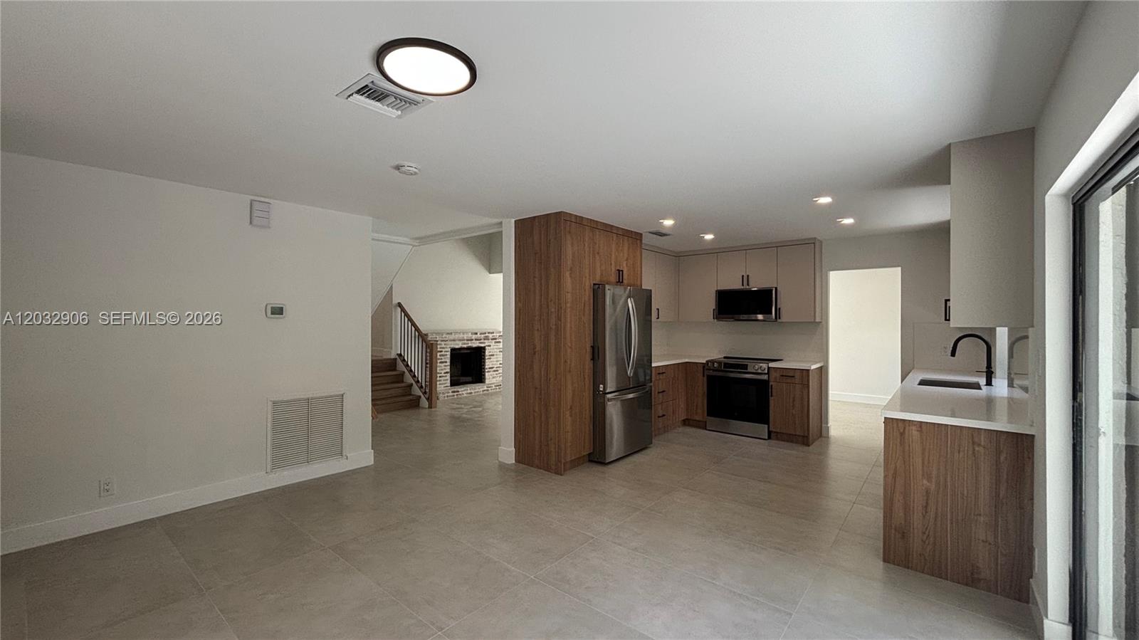A modern kitchen features wood-tone cabinetry, stainless steel appliances, and large light-colored floor tiles — 49 Forest Cir, Cooper City FL 33026, COOPER CITY, FL