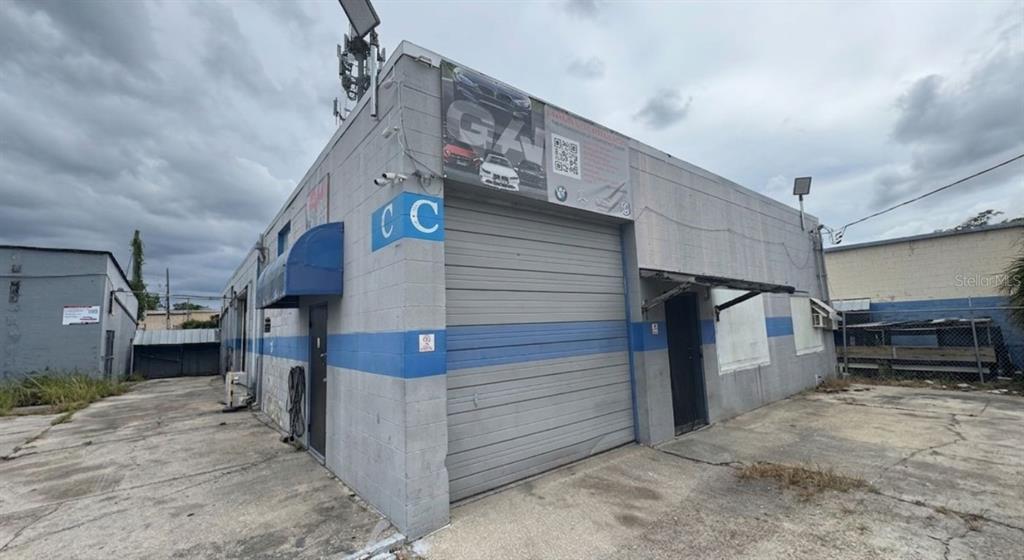 A gray industrial building with a roll-up garage door and a blue horizontal stripe — 4120 ROUSH AVENUE, ORLANDO, FL