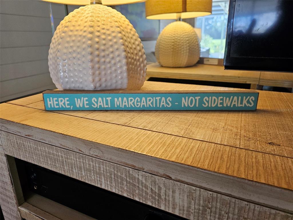 A decorative sign reading "Here, we salt margaritas - not sidewalks" sits on a wooden console table — 6147 43RD STREET W, BRADENTON, FL