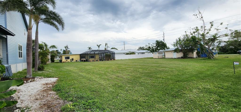 A large, grassy vacant lot is situated between several residential houses under a cloudy sky — 316 DURRANCE STREET, PUNTA GORDA, FL