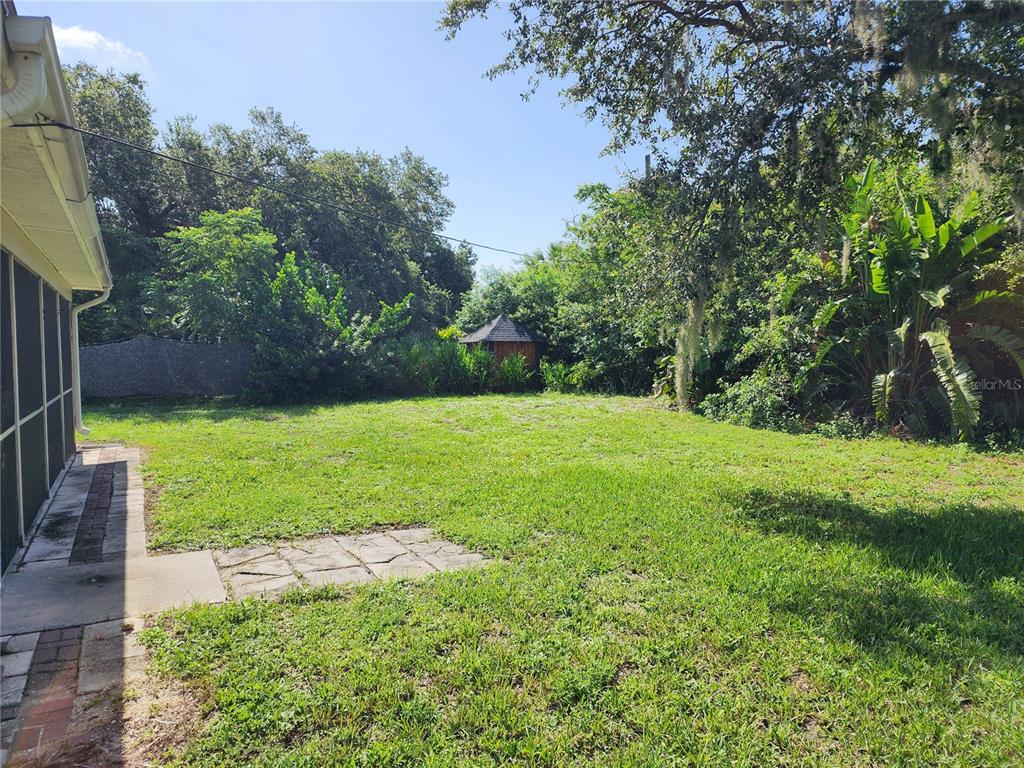 A grassy backyard features a small wooden shed, mature trees, and a screened-in patio area — 1225 ARMSDALE AVENUE, PORT CHARLOTTE, FL
