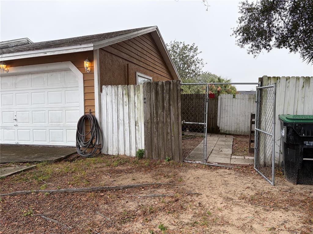 A side view of a house garage with a wooden fence and a metal gate — 1311 WOODMAN WAY, ORLANDO, FL