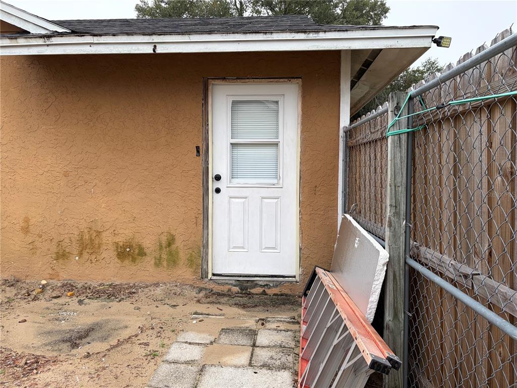 An exterior view of a white door on a stucco wall next to a fence — 1311 WOODMAN WAY, ORLANDO, FL