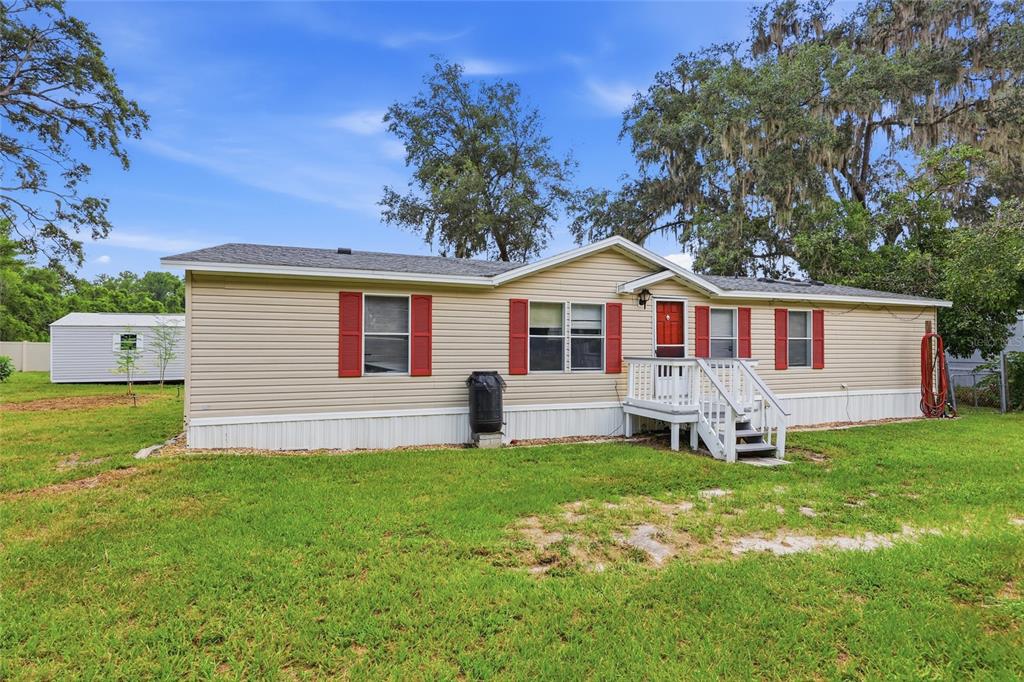 A single-story manufactured home with beige siding, red shutters, and a small white front porch — 7014 SW 49TH PLACE, GAINESVILLE, FL