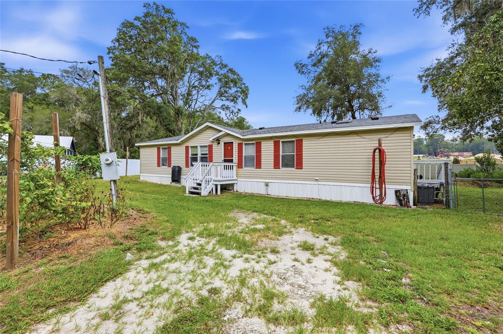 A tan manufactured home with red shutters sits on a grassy lot with a dirt driveway — 7014 SW 49TH PLACE, GAINESVILLE, FL
