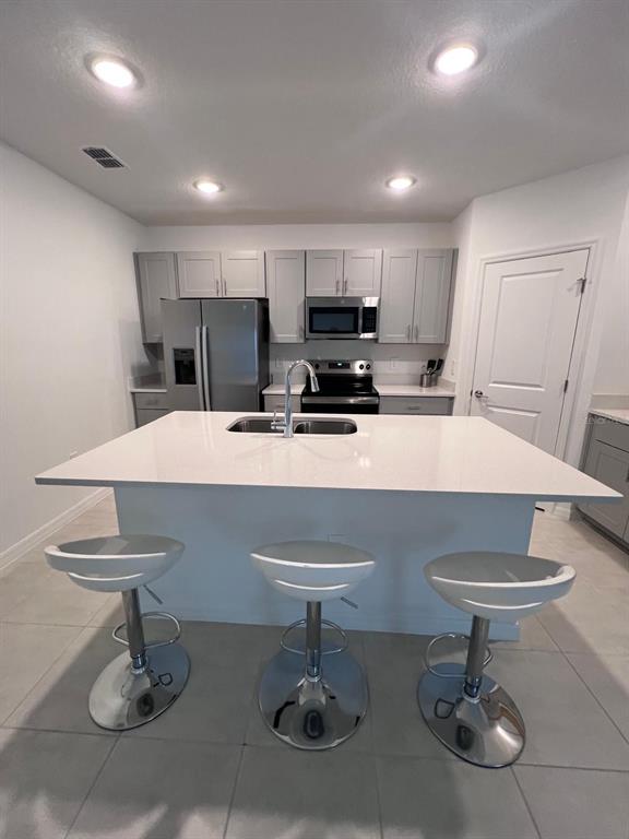A kitchen features a white island with three bar stools, stainless appliances, and gray cabinetry — 424 WAYLAND DRIVE, HAINES CITY, FL