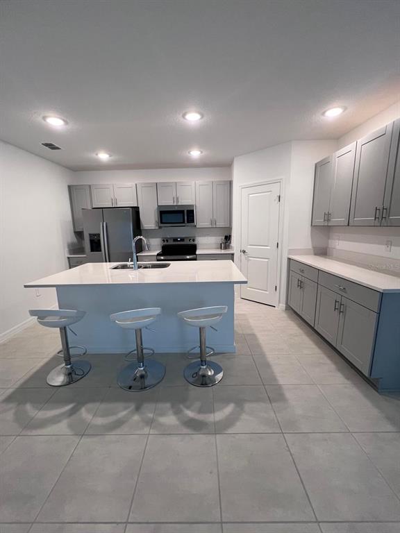 A kitchen features gray cabinetry, white countertops, a central island with three stools, and tile flooring — 424 WAYLAND DRIVE, HAINES CITY, FL
