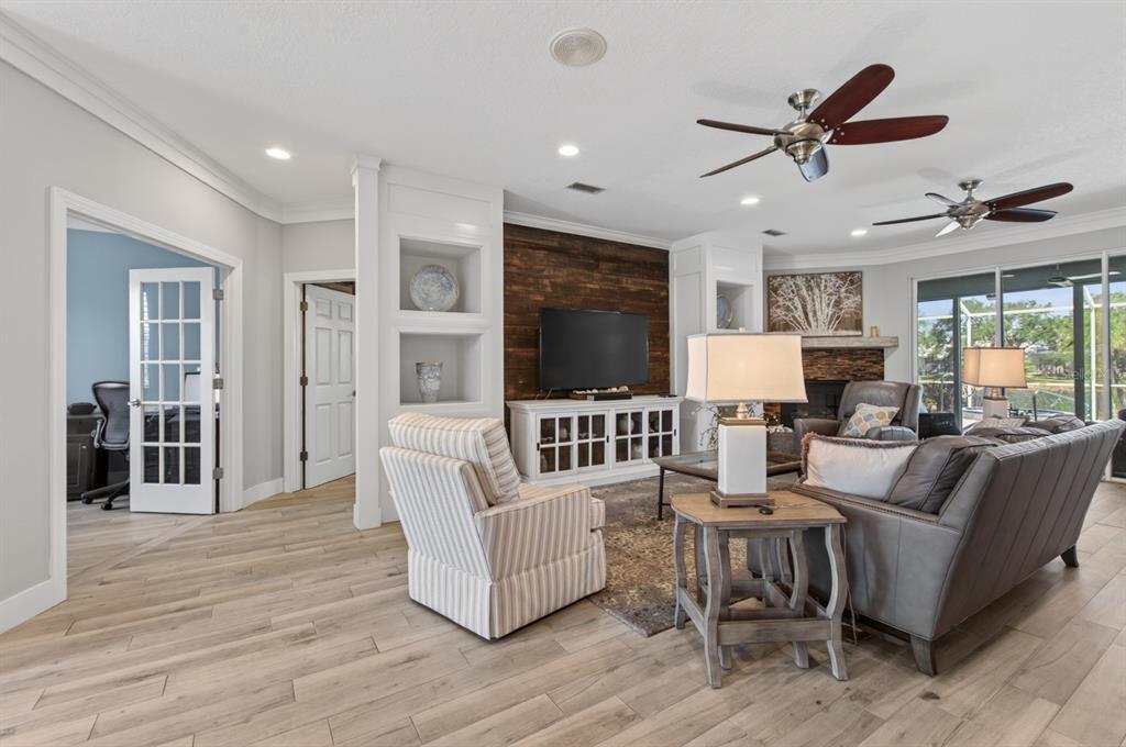 A living room features wood-look tile flooring, a wood-paneled accent wall, and two ceiling fans — 6119 9TH AVENUE CIRCLE NE, BRADENTON, FL