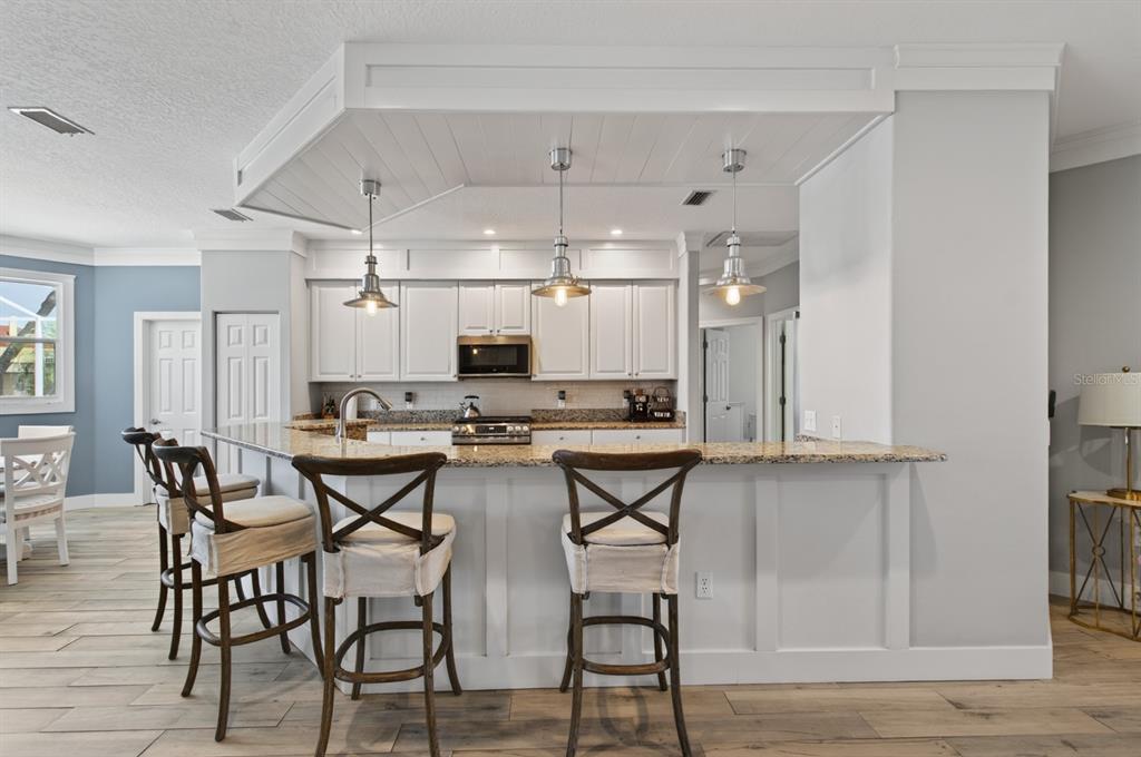 A kitchen features white cabinetry, granite countertops, a breakfast bar with stools, and pendant lighting — 6119 9TH AVENUE CIRCLE NE, BRADENTON, FL