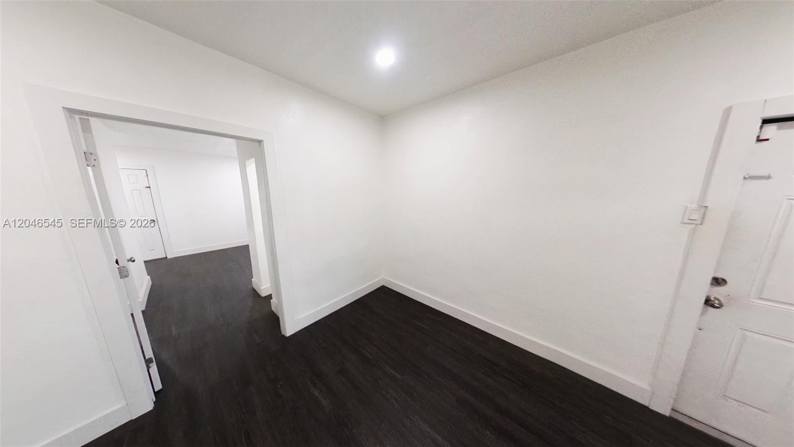 A small, empty room features white walls, dark wood-look flooring, and a white door — 1020 E 17th St # 1020, Hialeah FL 33010, HIALEAH, FL