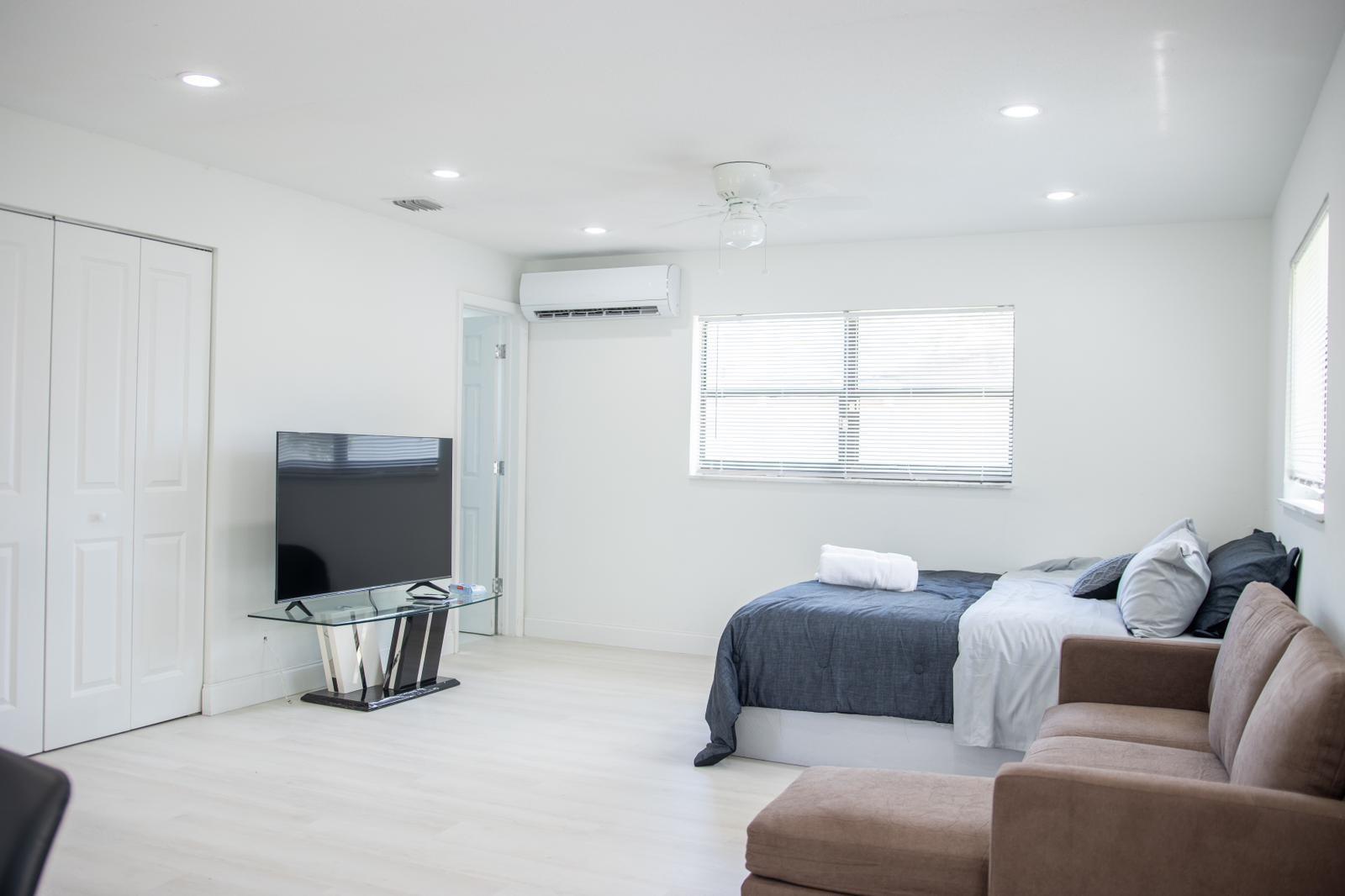 A bedroom with white walls, light flooring, a bed, a television, and a brown sofa — 320 NW 4th Avenue # 3, Deerfield Beach FL 33441, DEERFIELD BEACH, FL
