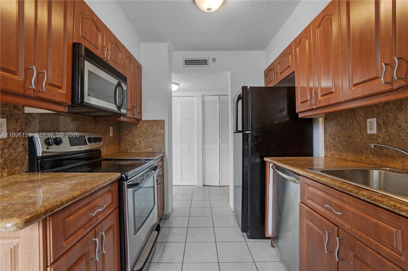 A galley kitchen features wood cabinets, granite countertops, and black and stainless steel appliances — 1688 West Ave # 408, Miami Beach FL 33139, MIAMI BEACH, FL