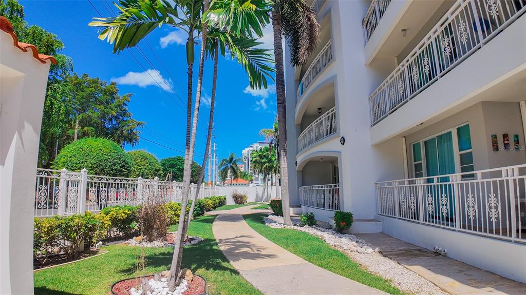 A paved walkway leads past a white multi-story apartment building with balconies and palm trees — PR-115 ENSENADA WARD RINCON WAVE VIEW UNIT 1B, RINCON, PR