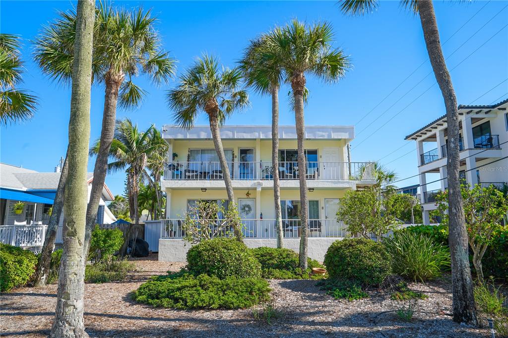 A two-story, light-yellow apartment building with balconies is surrounded by palm trees and landscaping — 108 14TH AVENUE UNIT 2, ST PETE BEACH, FL
