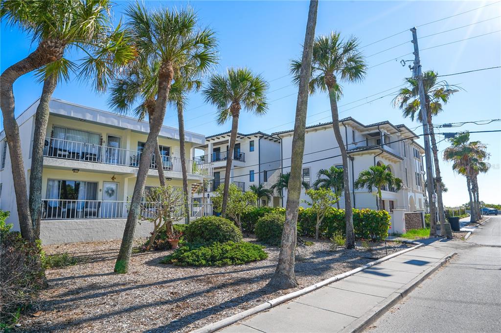 A street-level view of multi-story apartment buildings with palm trees and a sidewalk — 108 14TH AVENUE UNIT 2, ST PETE BEACH, FL