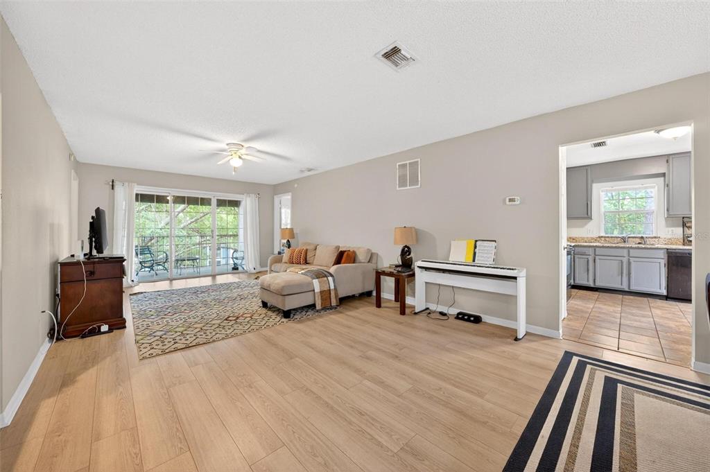 A living room with light wood flooring, a sectional sofa, and an adjacent kitchen — 7302 OLYMPIA COURT, LONGWOOD, FL