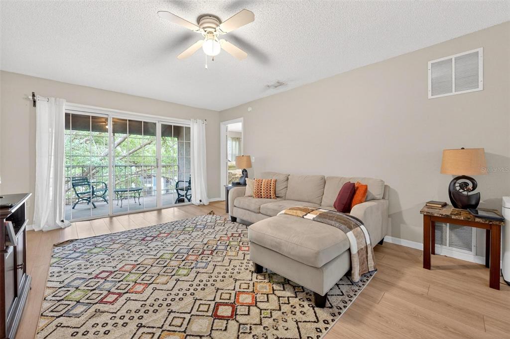 A living room features a beige sectional sofa, a patterned area rug, and sliding glass doors — 7302 OLYMPIA COURT, LONGWOOD, FL