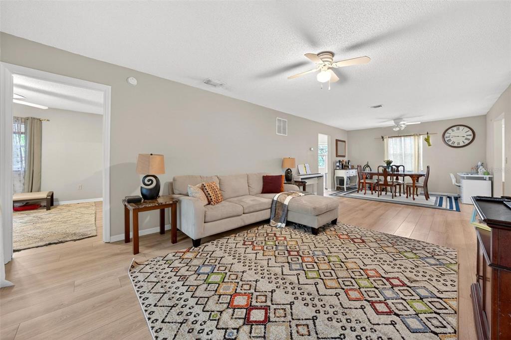 A living room with light-colored walls, wood-look flooring, a patterned area rug, and dining area — 7302 OLYMPIA COURT, LONGWOOD, FL