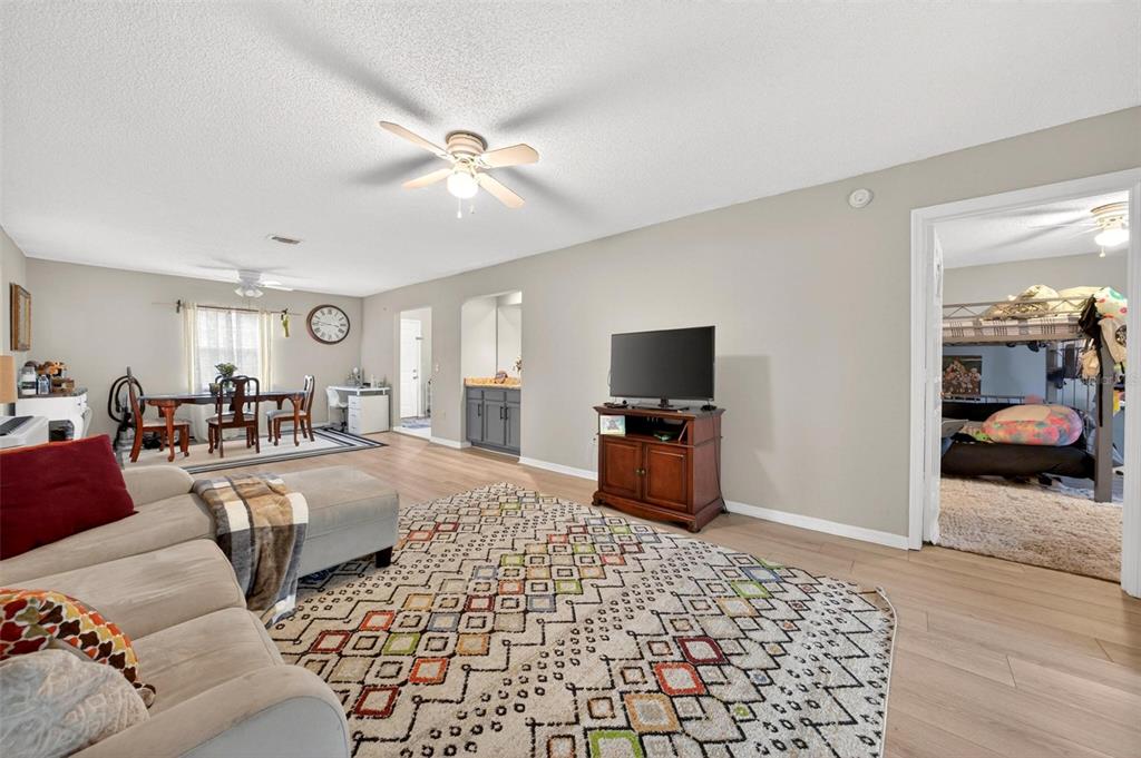 A living room with light wood floors, a patterned rug, and an adjacent dining area — 7302 OLYMPIA COURT, LONGWOOD, FL