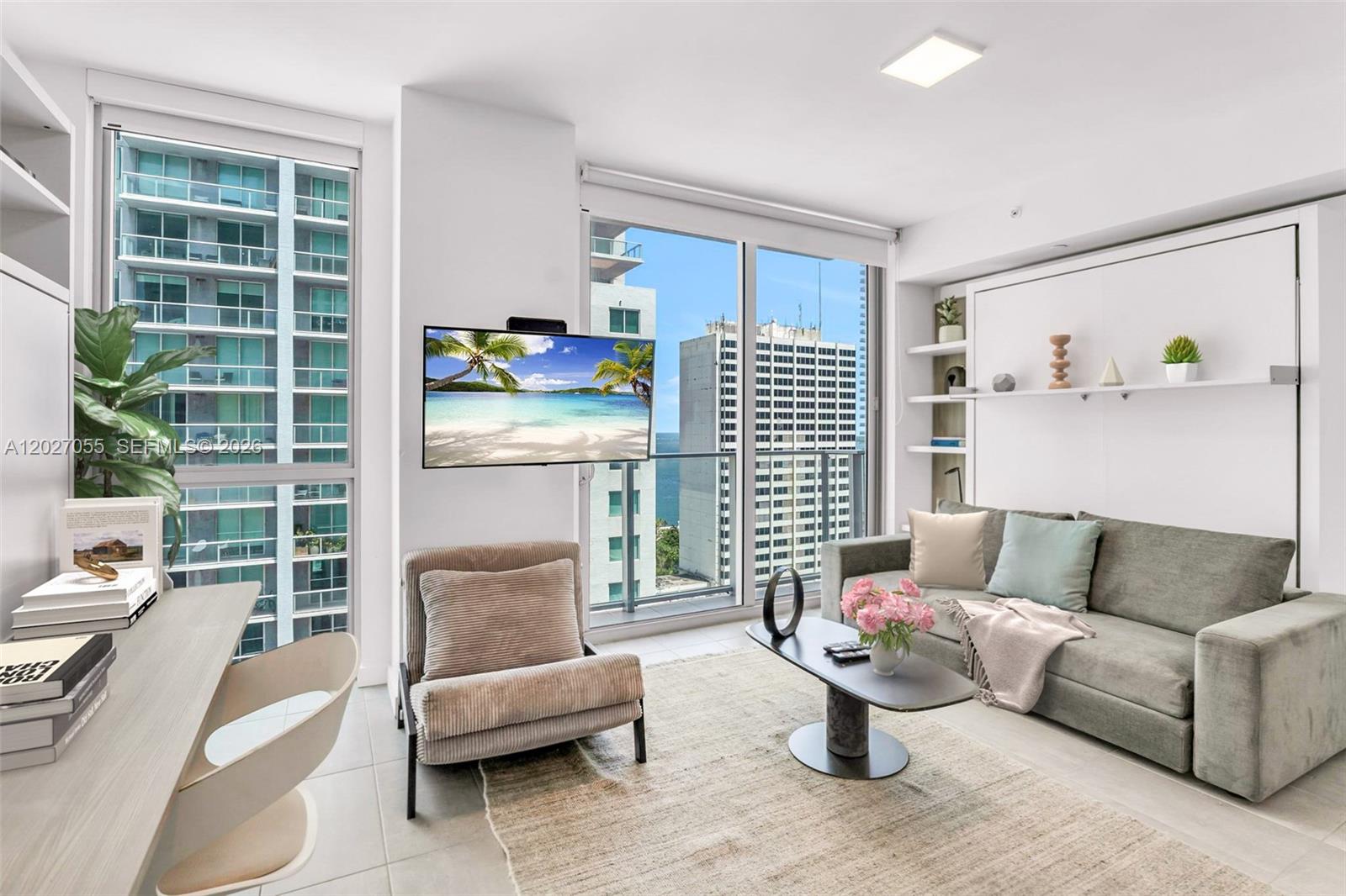 A modern living room features a sofa, a wall-mounted television, and floor-to-ceiling windows — 227 NE 2nd St # 2611, Miami FL 33132, MIAMI, FL