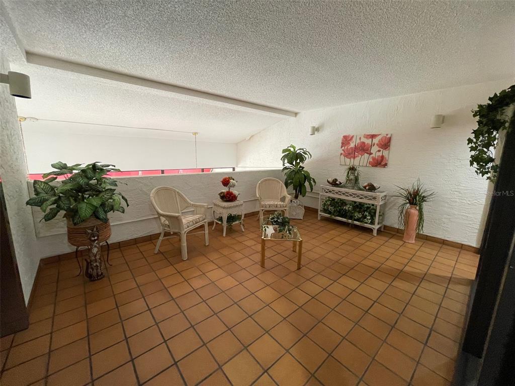 A covered balcony features terracotta tile flooring, white textured walls, and wicker patio furniture — 2591 COUNTRYSIDE BOULEVARD UNIT 5203, CLEARWATER, FL