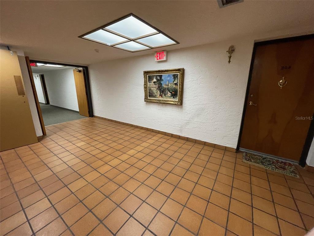 A tiled hallway features a framed painting, an exit sign, and a door labeled 308 — 2591 COUNTRYSIDE BOULEVARD UNIT 5203, CLEARWATER, FL