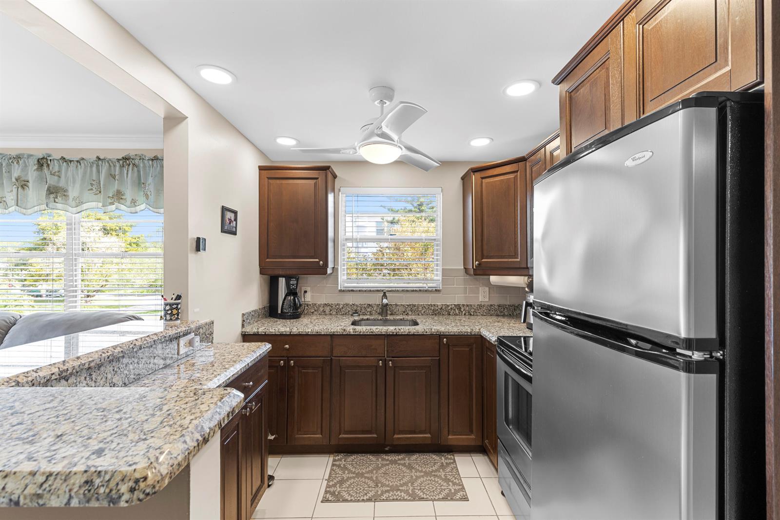 A kitchen features dark wood cabinets, granite countertops, stainless steel appliances, and a ceiling fan — 3024 Durham A, Deerfield Beach FL 33442, DEERFIELD BEACH, FL