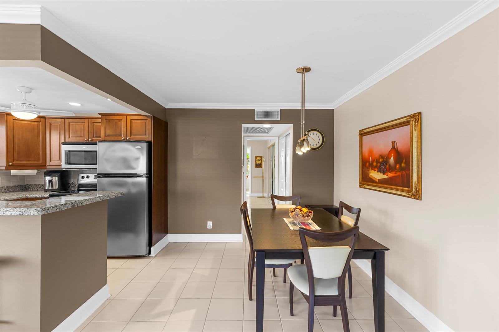 A dining area with a dark wood table and chairs sits adjacent to a kitchen — 3024 Durham A, Deerfield Beach FL 33442, DEERFIELD BEACH, FL