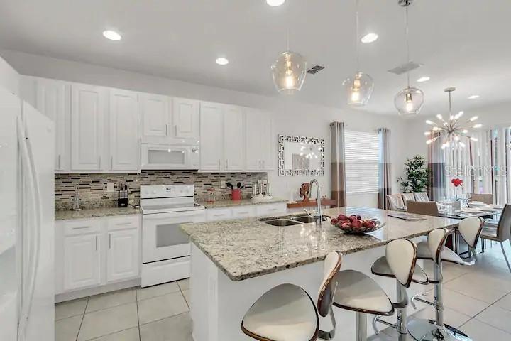 A kitchen features white cabinetry, granite countertops, a central island, and modern pendant lighting — 2669 CALISTOGA AVENUE, KISSIMMEE, FL