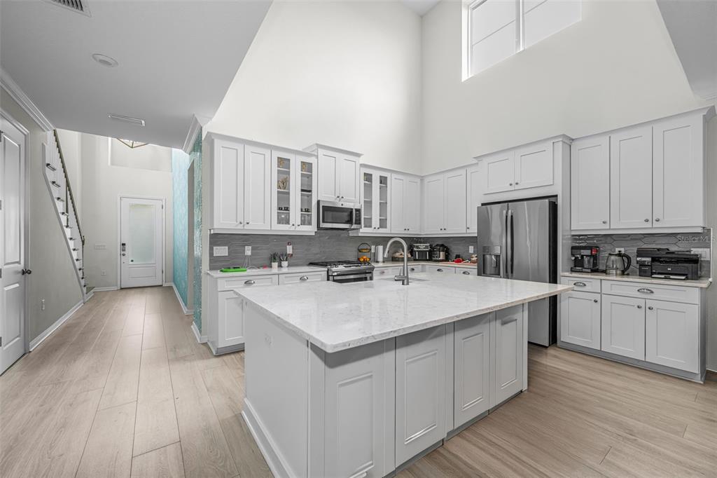 A modern kitchen features white cabinetry, a large marble-topped island, and high vaulted ceilings — 13760 STEVENSON LANE, ODESSA, FL