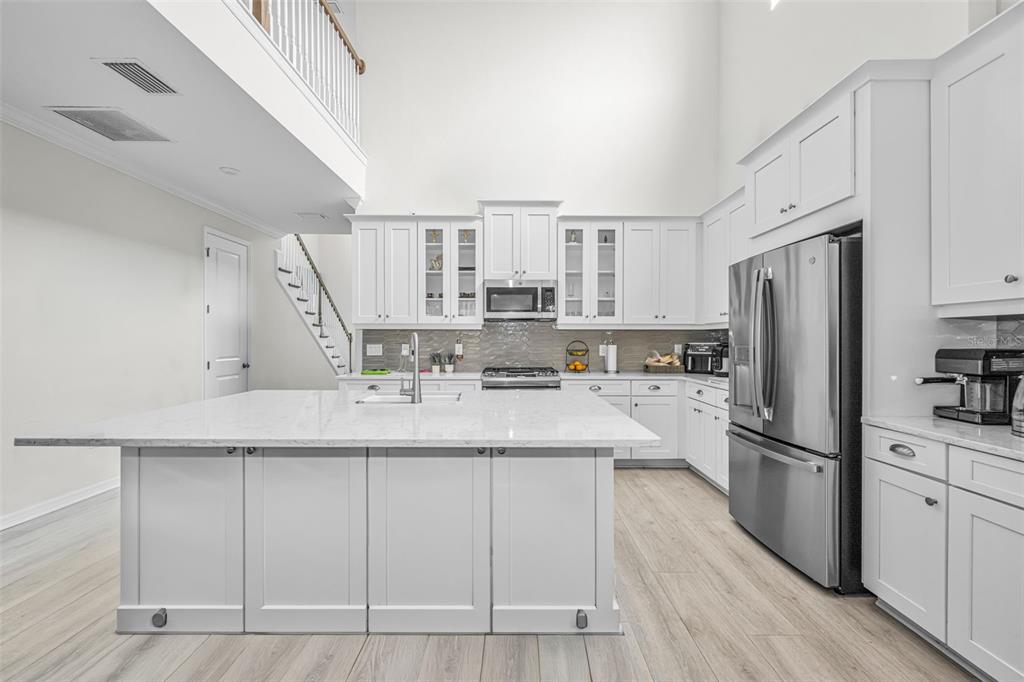 A modern kitchen features white cabinetry, a large marble-topped island, and stainless steel appliances — 13760 STEVENSON LANE, ODESSA, FL