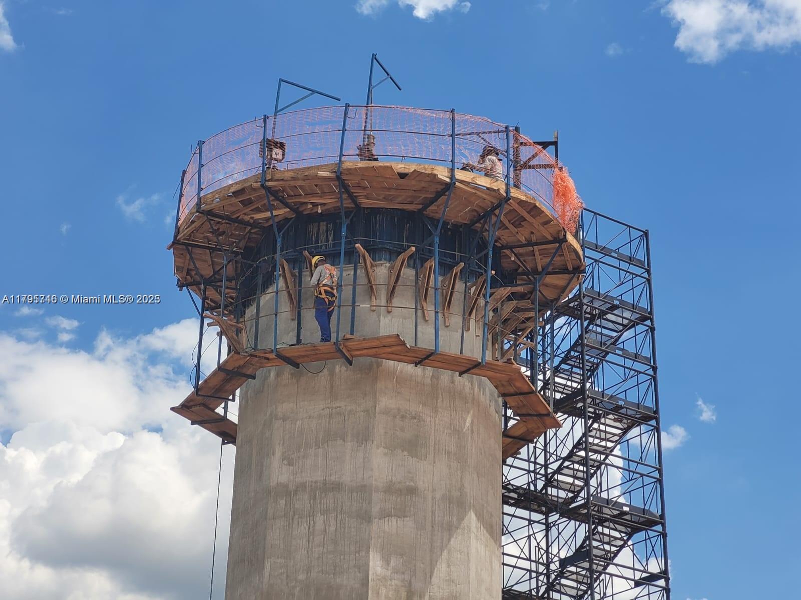 A construction worker stands on a wooden platform surrounding the top of a concrete tower — Cardeal Elias Fausto, SP, SP