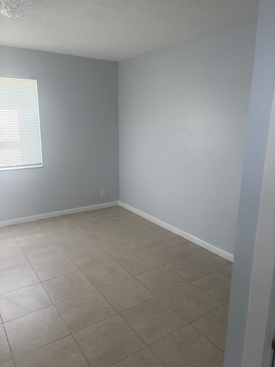 An empty bedroom features light blue walls, beige tile flooring, and a single window — FORT LAUDERDALE, FL