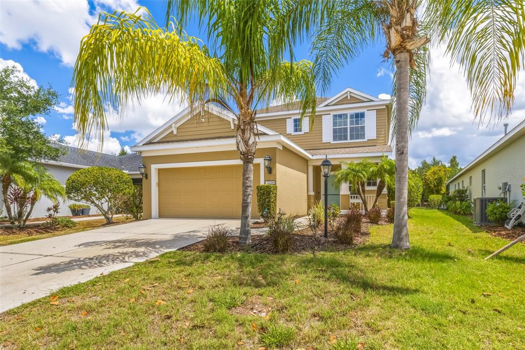 A two-story suburban house with a tan exterior, a two-car garage, and palm trees — 12224 LONGVIEW LAKE CIRCLE, BRADENTON, FL