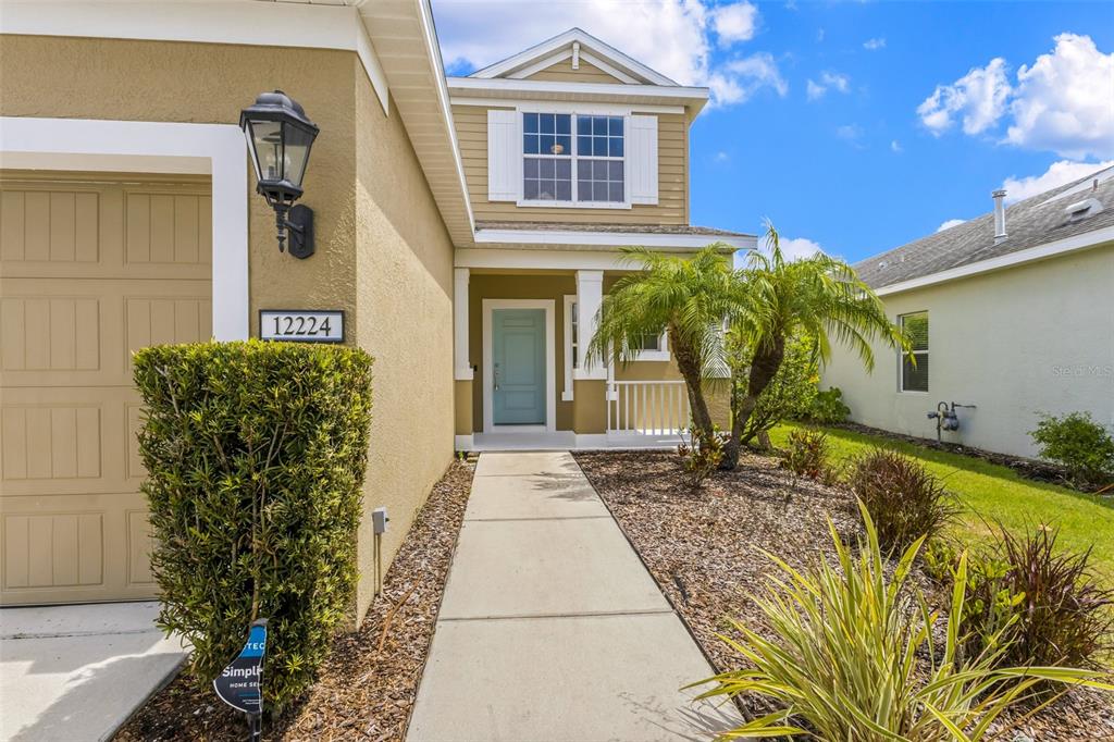 A tan house exterior features a light blue front door, a walkway, and landscaping — 12224 LONGVIEW LAKE CIRCLE, BRADENTON, FL