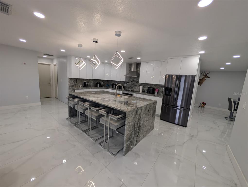 A modern kitchen features a large granite island, white cabinetry, and white marble-look tile flooring — 718 PARK MANOR DRIVE, ORLANDO, FL