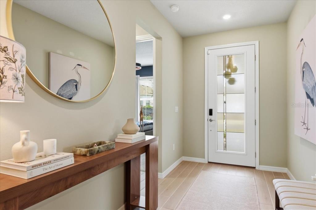 A bright entryway features a wooden console table, a round mirror, and a glass-paneled door — 15142 WILLOW RIDGE DRIVE, MONTVERDE, FL
