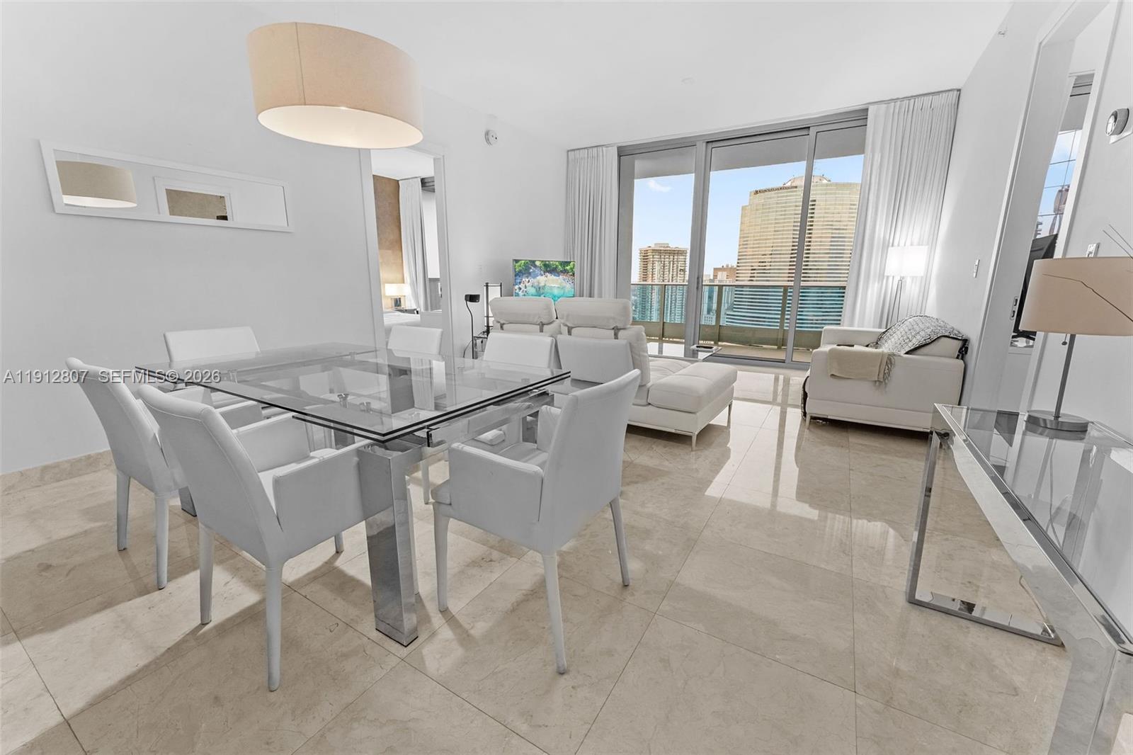 A modern dining and living area features white furniture, a glass table, and city views — 200 Biscayne Boulevard Way # 4510, Miami FL 33131, MIAMI, FL