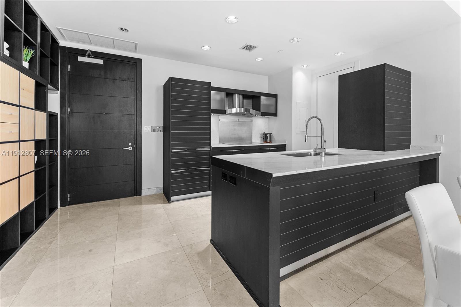 A modern kitchen features dark horizontal-slatted cabinetry, a marble-topped island, and light tile flooring — 200 Biscayne Boulevard Way # 4510, Miami FL 33131, MIAMI, FL