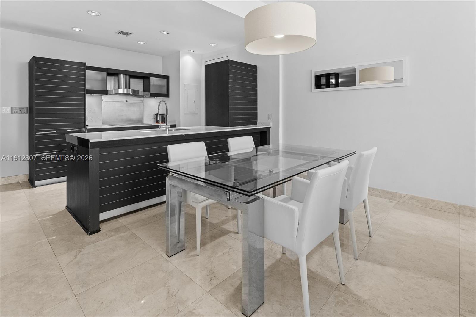A modern kitchen and dining area feature dark cabinetry, a glass table, and tile flooring — 200 Biscayne Boulevard Way # 4510, Miami FL 33131, MIAMI, FL