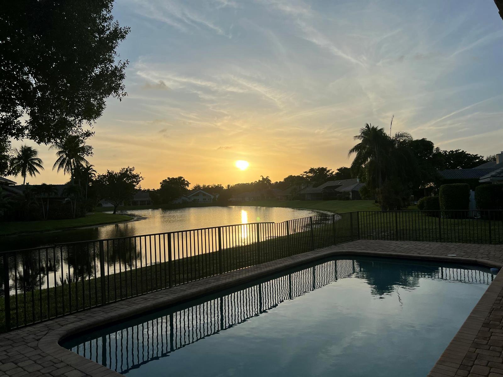 A backyard swimming pool overlooks a lake at sunset with a black metal fence — 3110 Equestrian Drive, Boca Raton FL 33434, BOCA RATON, FL