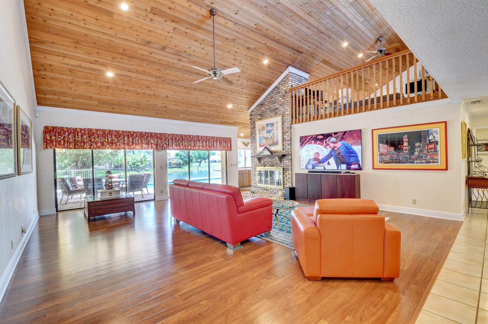 A living room features a vaulted wood-plank ceiling, brick fireplace, and red and orange furniture — 3110 Equestrian Drive, Boca Raton FL 33434, BOCA RATON, FL