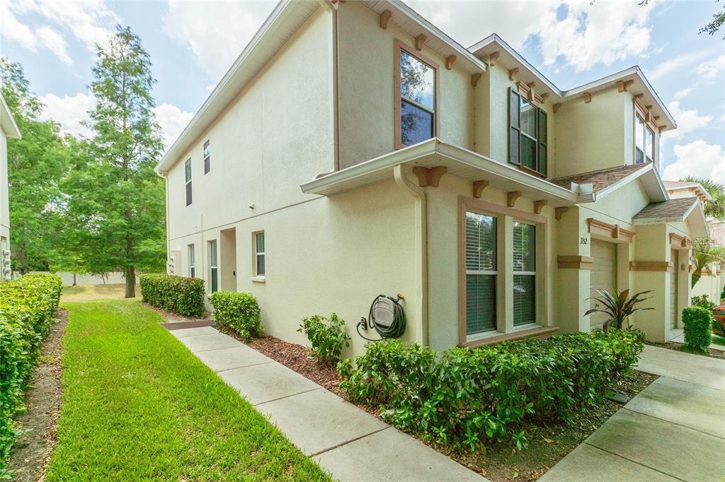 A two-story beige townhouse exterior features a side walkway, green landscaping, and a garden hose — 3152 ROYAL TUSCAN LANE, VALRICO, FL