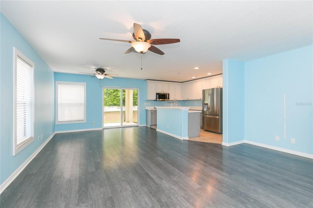 An open-concept living area with light blue walls, gray wood flooring, and a kitchen island — 3152 ROYAL TUSCAN LANE, VALRICO, FL