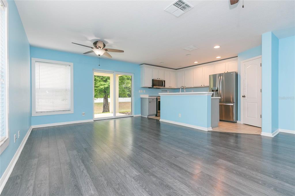 A bright blue living room with gray wood floors opens to a kitchen with white cabinets — 3152 ROYAL TUSCAN LANE, VALRICO, FL